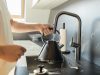 Person füllt einen Wasserkocher am Küchenhahn mit frischem Leitungswasser.