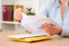 Close up of woman hands putting a letter inside an envelope on a desk at home or office