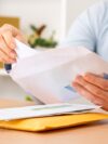 Close up of woman hands putting a letter inside an envelope on a desk at home or office